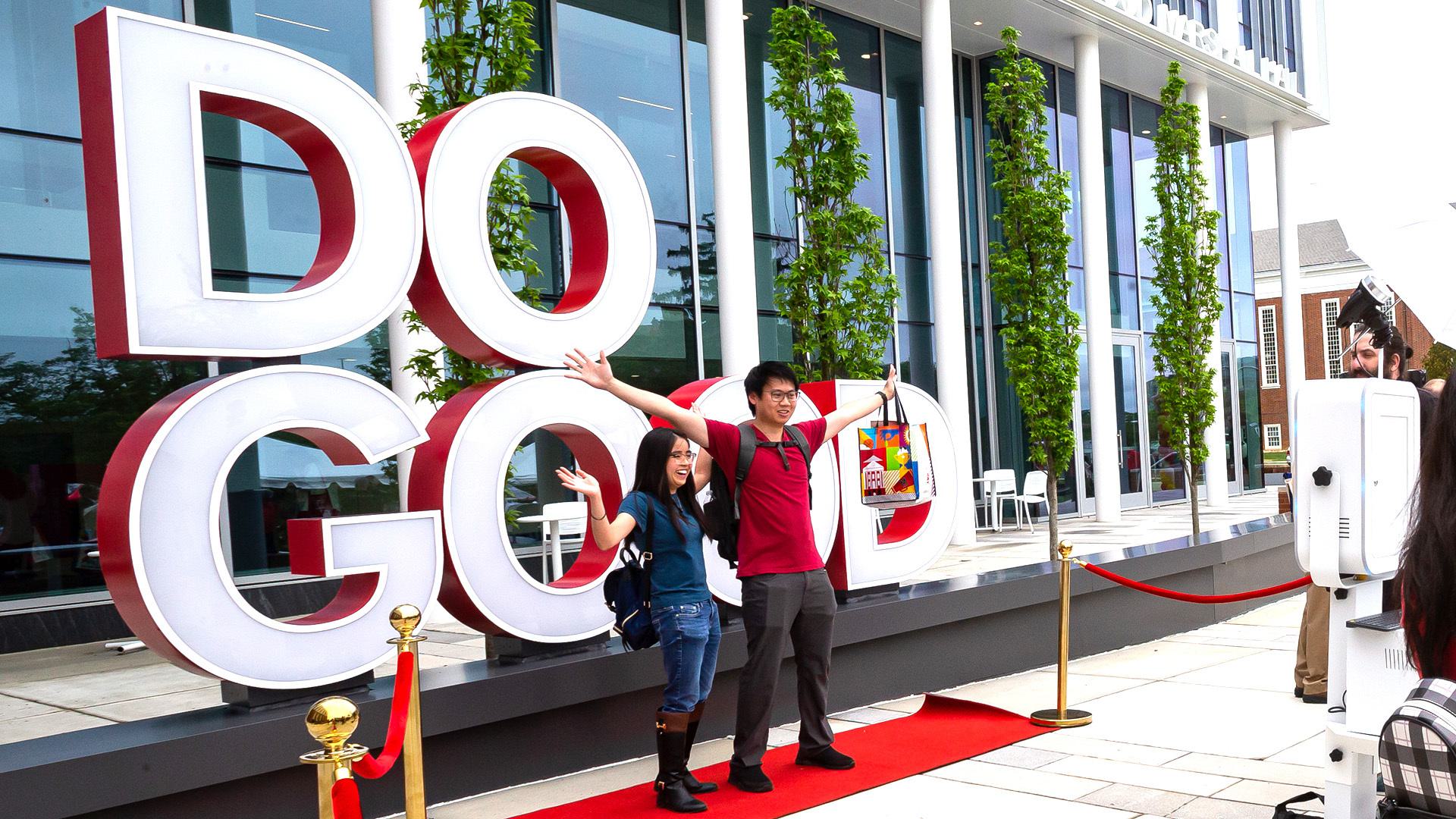 Two students pose in front of a large statue that reads, "Do Good."