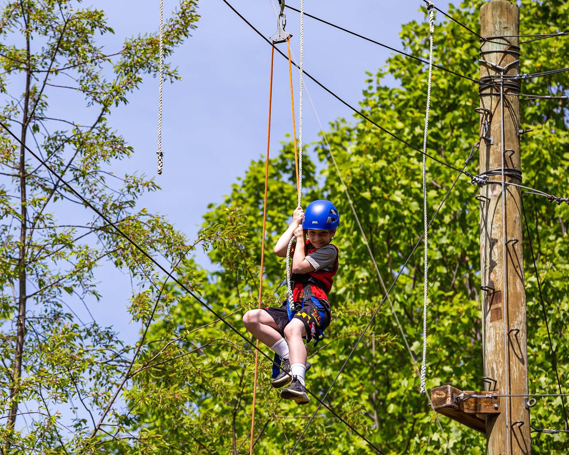 A child in a blue helmet slides across the zipline at the Eppley Recreation Center Challenge Course on campus.